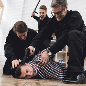 Three men in black shirts and pants restraining a man on the floor.