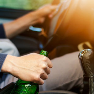 A man holding a beer bottle while driving a car, illustrating the consequences of DUI cases in California. - Manavi Law Group, APLC