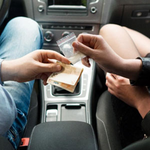 Boy and girl in car exchanging drugs and money, depicting a drug deal - Manavi Law Group